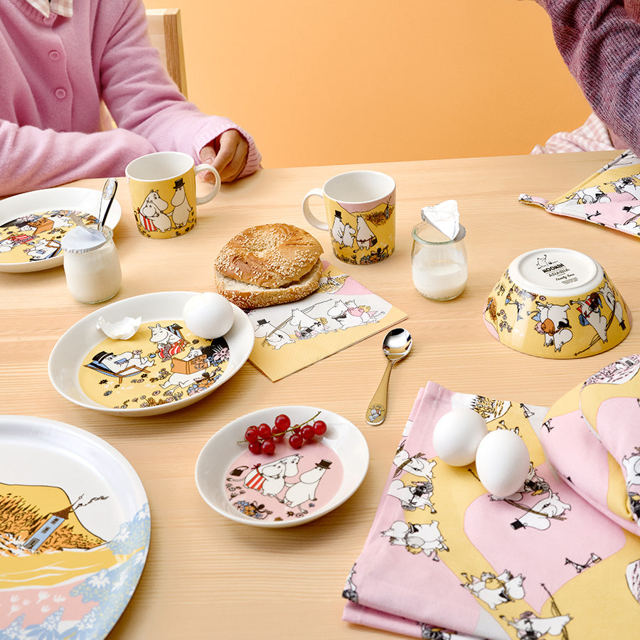 Søtt frokostbord med Moomin Arabia Mummi asjett 15cm Familietid, sammen med matchende kopper og skåler, ideelt for koselige måltider.