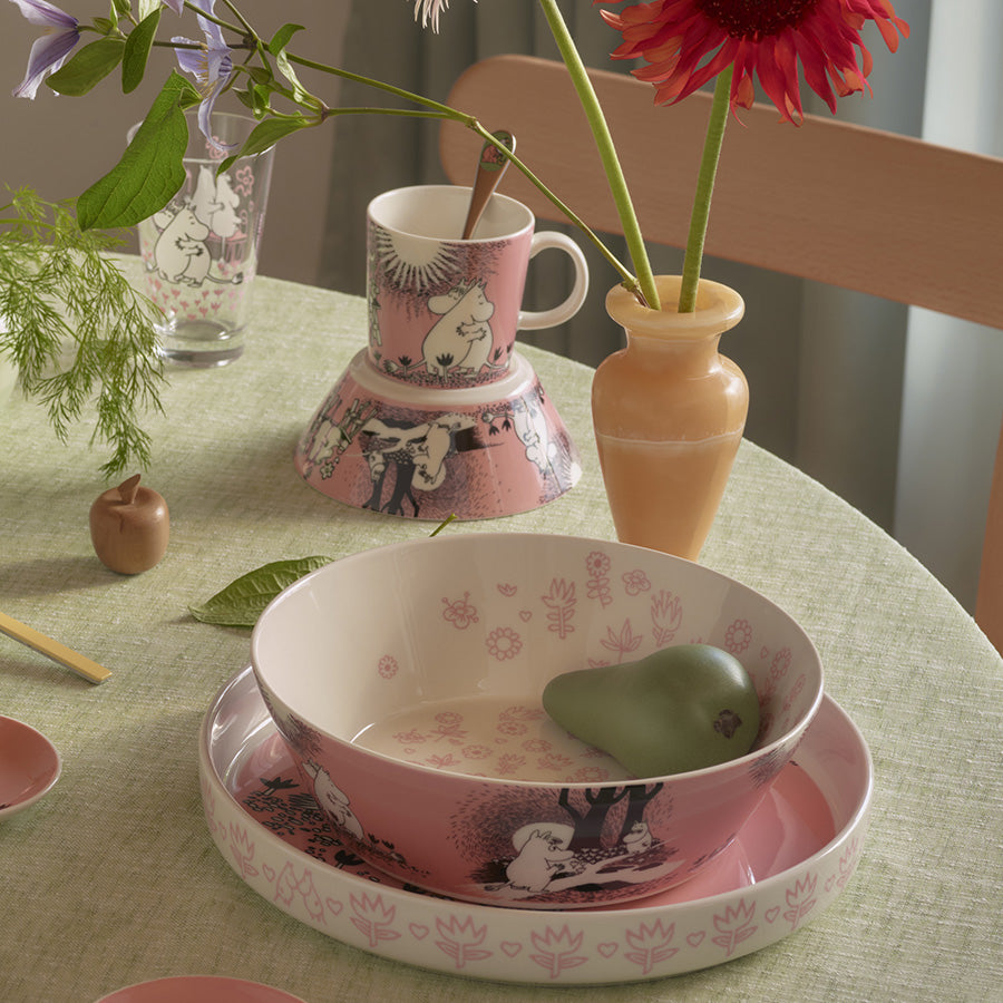 Ildfaste skåler og kopper med Moomin-design, inkludert en paiform på bordet, som viser en koselig middagsscene.