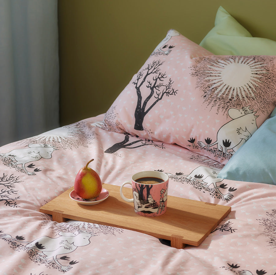 Mummi kopp plassert på en seng sammen med en tallerken og en pære, ideelt for en avslappende morgen.