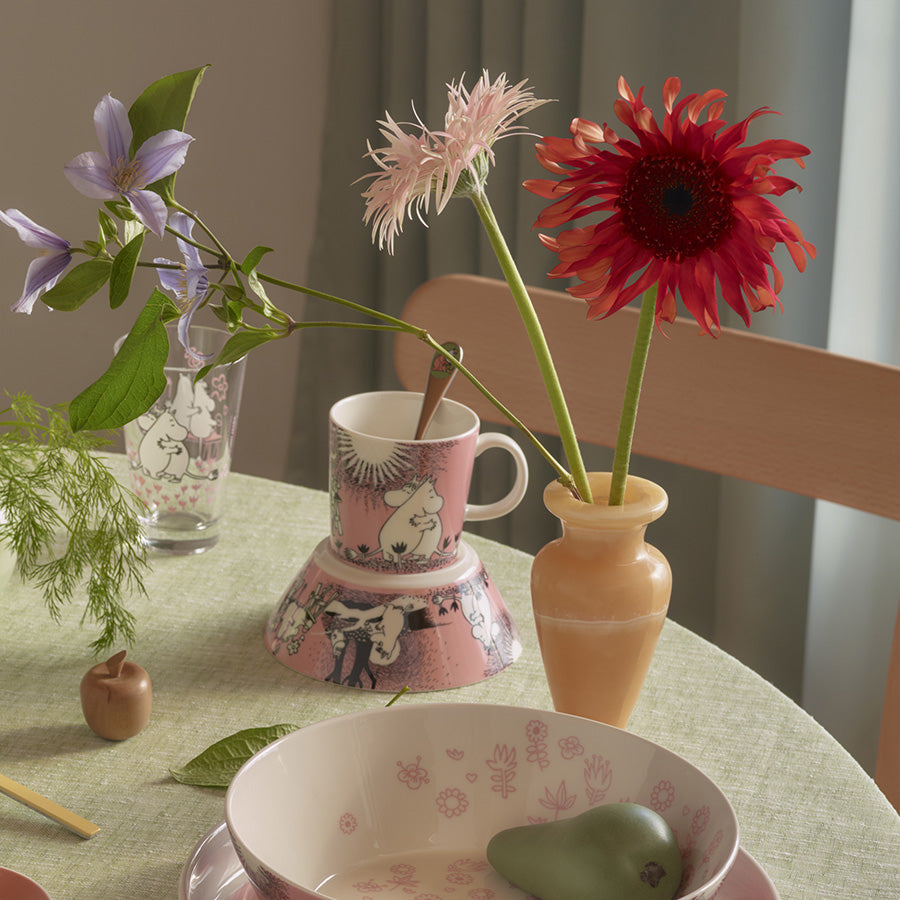 Mummi kopp dekorert med blomster og plassert på et bord sammen med en vase, gir et livlig og vennlig preg.