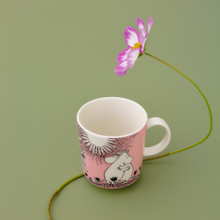 Mummi kopp med design av Mummitrollet, omfavnet av en blomst, gir et kunstnerisk inntrykk.