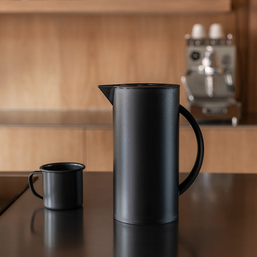 Sort termokanne ved siden av en kopp, designet for å gi deg varm kaffe hele dagen.
