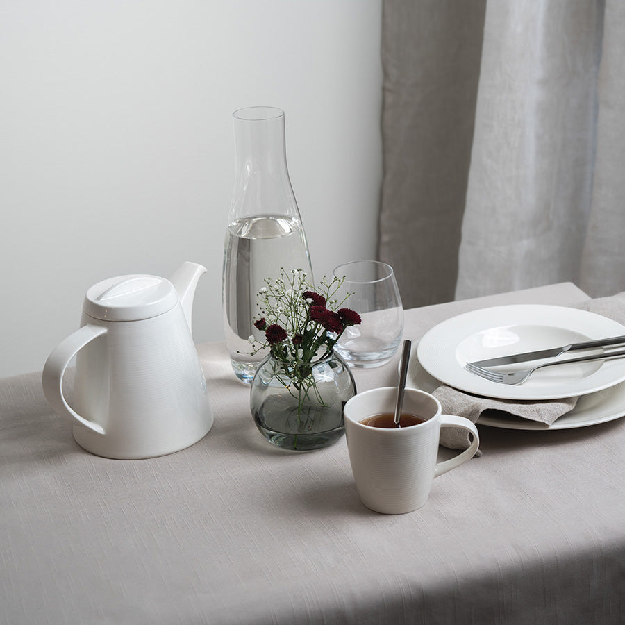 Elegant borddekorasjon med tekanne, glassvannkaraf, og kopper, perfekt for servering av te.