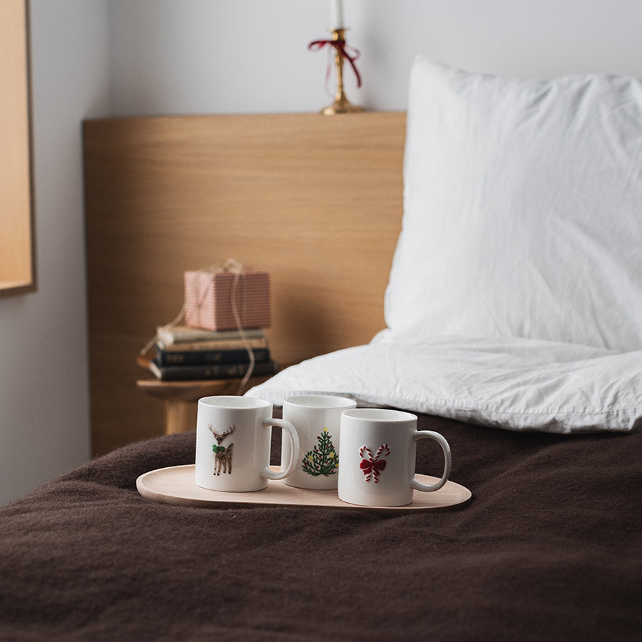 Christiania 1739 Julekolleksjon krus, sammen med andre julekrus på et sengesett i et koselig vintermiljø.