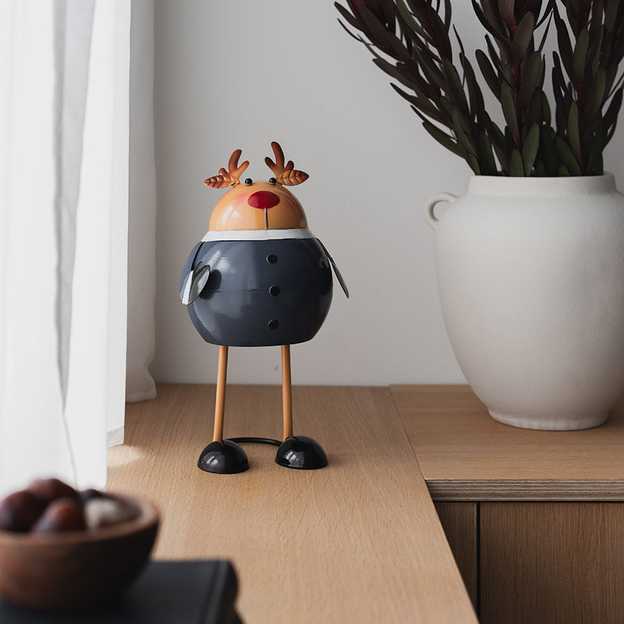 Christiania 1739 Julekolleksjon Figur Reinsdyr 18cm, dekorativ reinsdyrfigur plassert på et moderne møbel, omgiven av planter og naturlig lys.