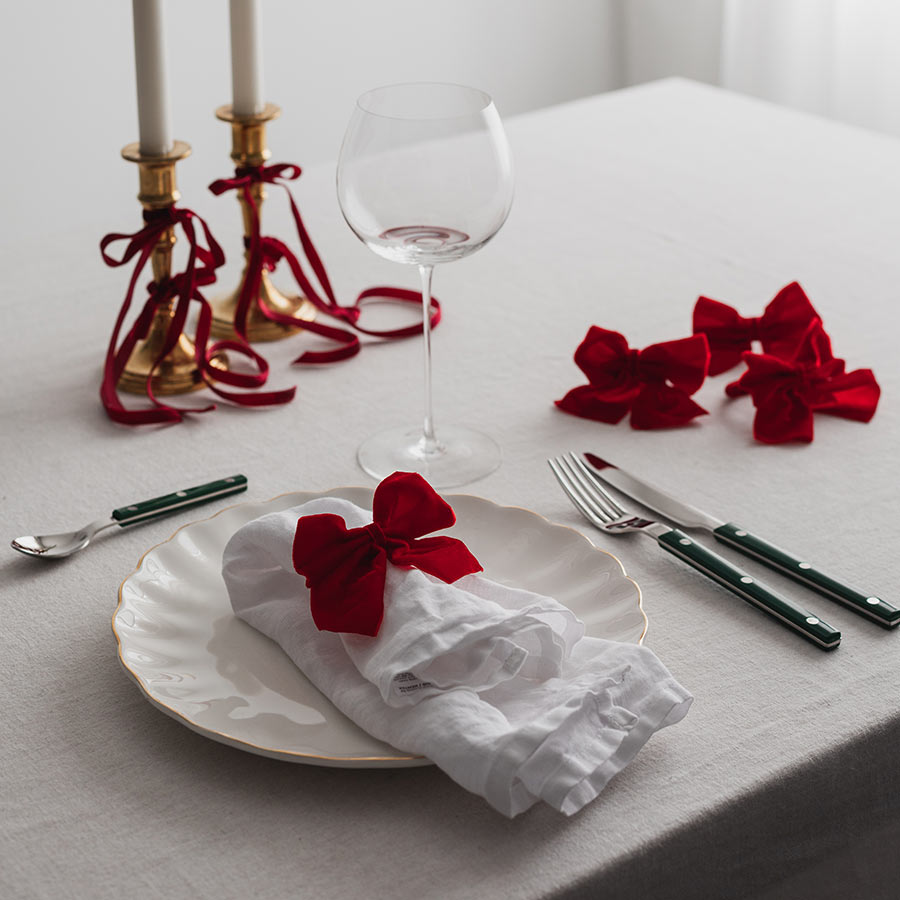 Juledekket bord med Christiania 1739 serviettringer in rød sløyfe, hvor servietter og glass skaper en festlig atmosfære.