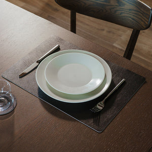 Svart spisebrikke på spisebord med tallerken, bestikk og glass i elegant borddekking