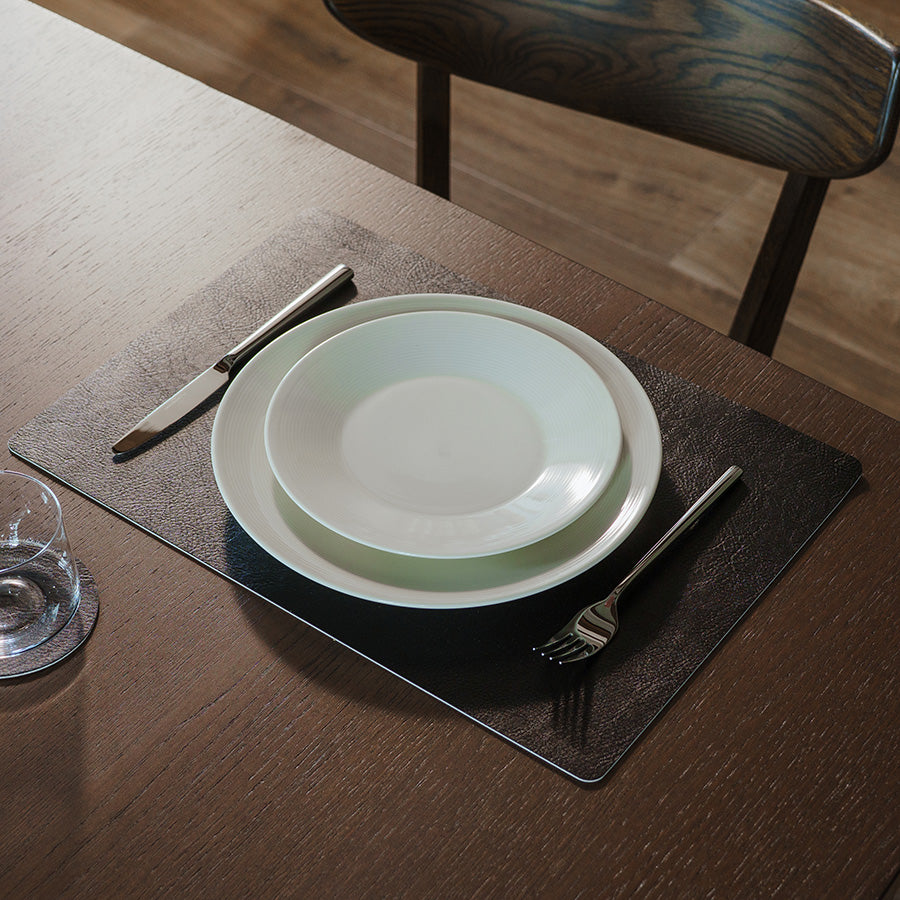 Svart spisebrikke på spisebord med tallerken, bestikk og glass i elegant borddekking
