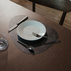 Svart eggformet spisebrikke på spisebord med tallerken, bestikk og glass