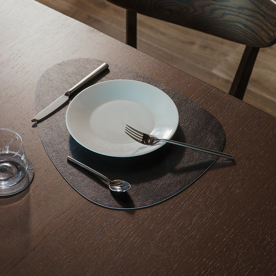 Svart eggformet spisebrikke på spisebord med tallerken, bestikk og glass