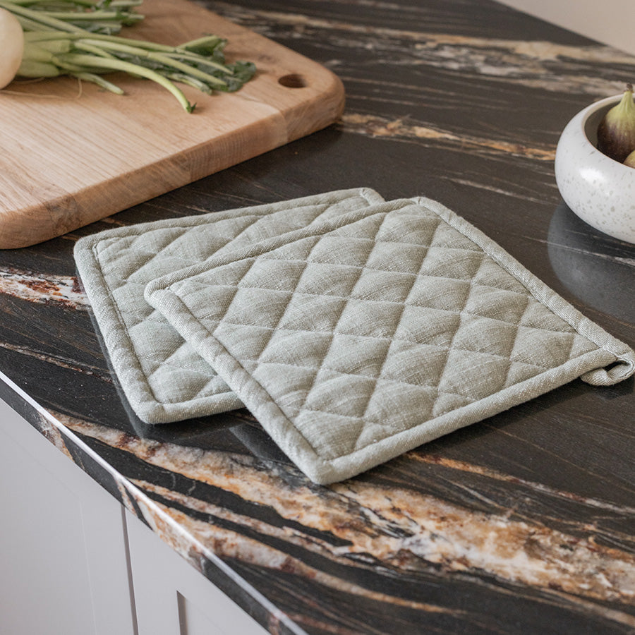 Sett med tre grønne grytekluter i 100% bomull, vasket look, plassert på en moderne kjøkkenbenk med mørke marmoroverflater.