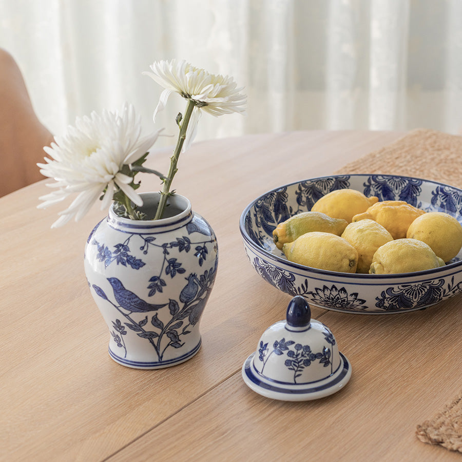 Mingkrukke med lokk, sammen med en skål med sitroner, viser stilen og bruk av krukken i hjemmet som pynt. Blomster i krukken fremhever det klassiske designet.
