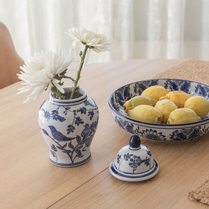 Mingkrukke med lokk, sammen med en skål med sitroner, viser stilen og bruk av krukken i hjemmet som pynt. Blomster i krukken fremhever det klassiske designet.