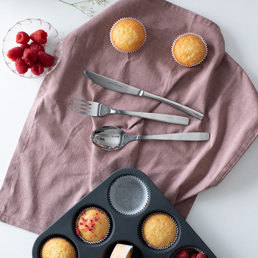 Christiania Bestikk Torino bestikk med kniv, gaffel og skje på linserviett sammen med nybakte muffins