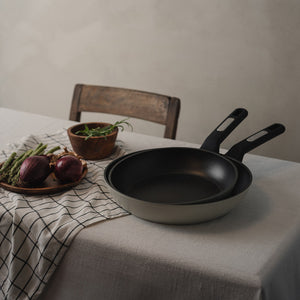 Christiania 1739 Plus Stekepanne 28cm Beige - To stekepanner plassert på et bord, fremhever det stilrene designet og allsidigheten til stekepannen.