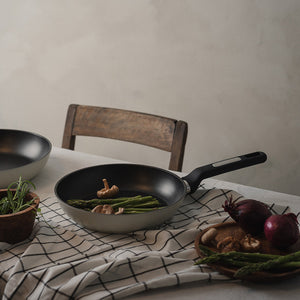 Christiania 1739 Plus Stekepanne 24cm Beige med grønnsaker som asparges og sopp på en matbord, illustrerer praktisk bruk av stekepannen.