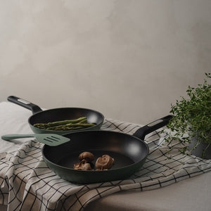 To Christiania 1739 Plus Stekepanner 28cm Grønn på et dekket bord, med grønnsaker som asparges og sopp.