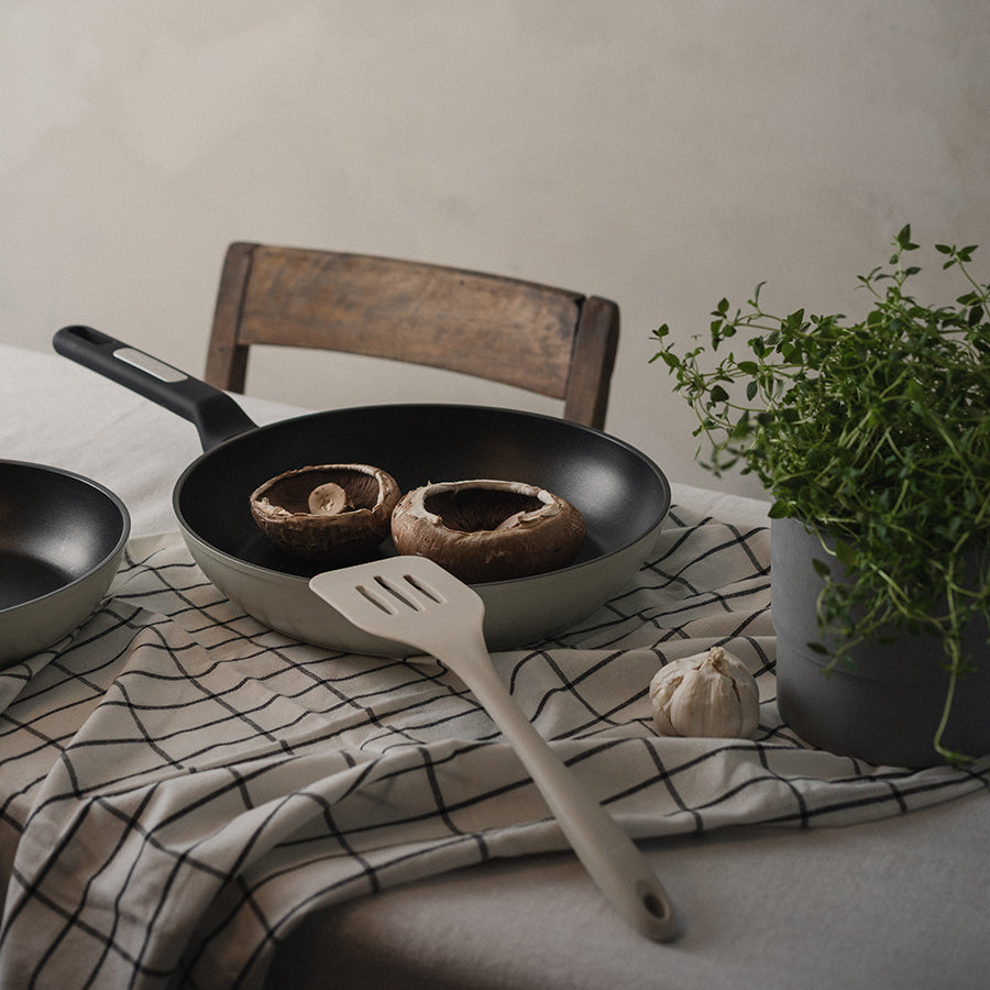 Christiania 1739 Plus Stekespade Silikon Beige i bruk med sopp og hvitløk i en stekepanne, viser den fleksible og skånsomme designen.