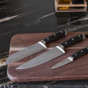 Tre ClassicPro santokukniver i rustfritt stål på et skjærebrett, ideelle for hakking og skjæring av grønnsaker og kjøtt.
