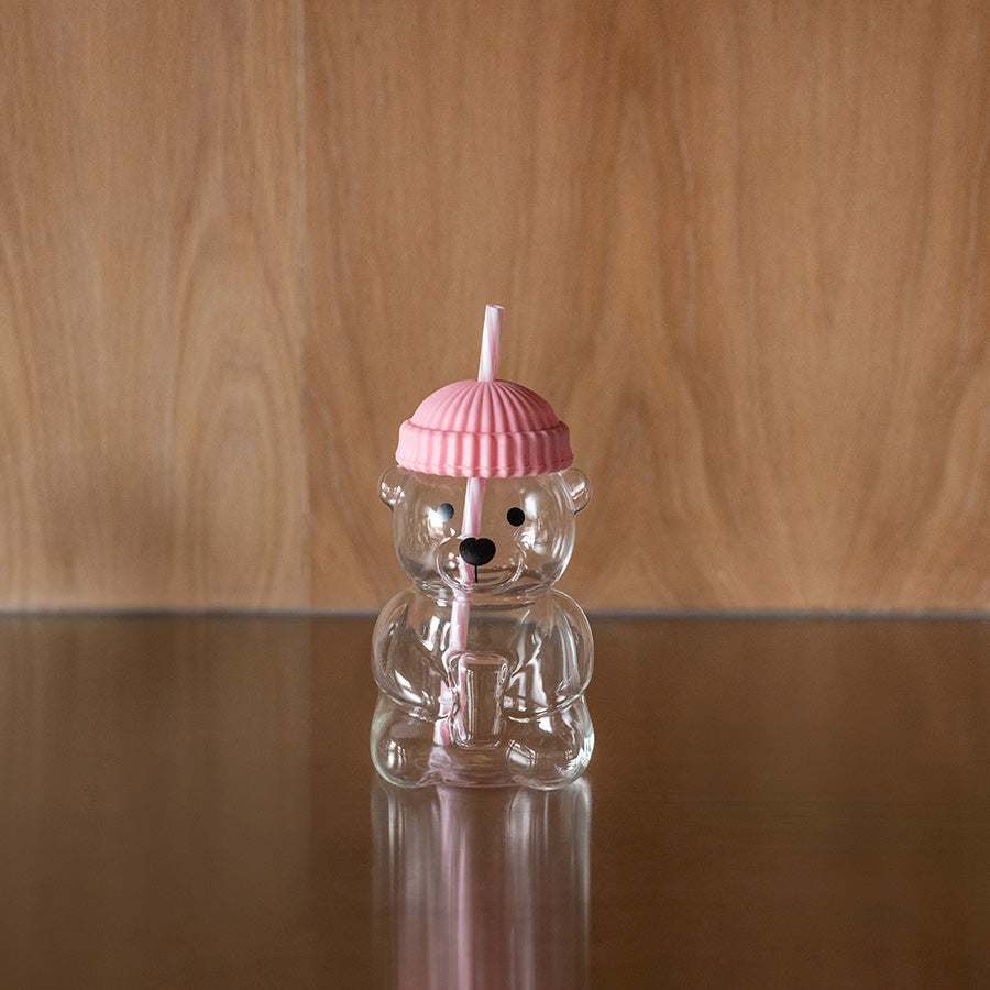 Nærbilde av bjørneformet glass med rosa silikonhatt og sugerør. Lekent design for barn og voksne.