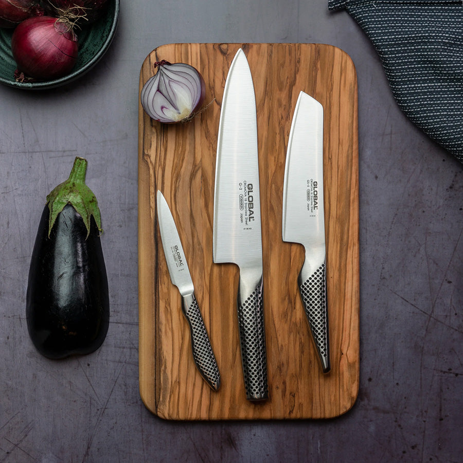 Tre Global kniver på skjærebrett med aubergine, løk og grønnsaker