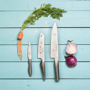 Global kniver på blått kjøkkenbord med gulrot, urter og løk