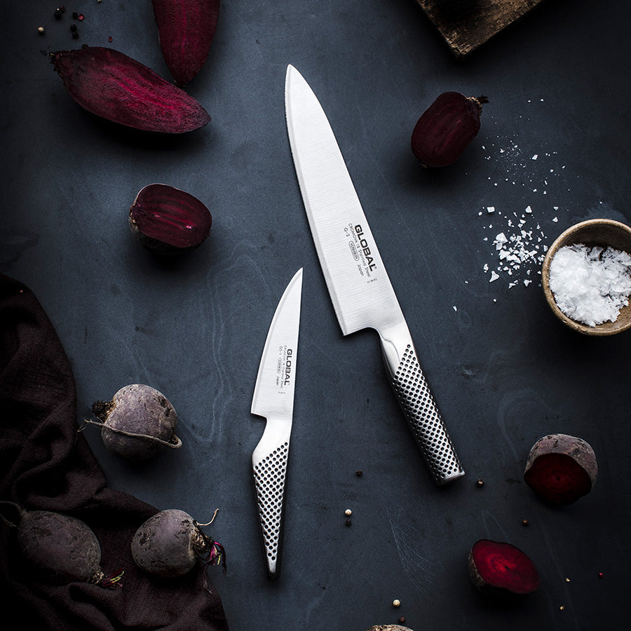 Global knivsett bestående av kokkekniv G-2 og universalkniv GS-1, plassert på en mørk overflate med rødbeter, perfekt for hjemmekokker.