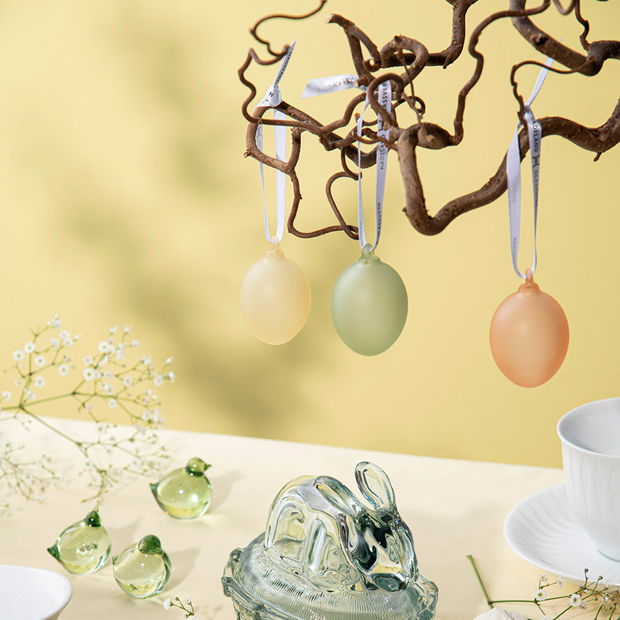 Frostede glassegg hengende på en gren, i delikate farger, som skaper en elegant påskeatmosfære.