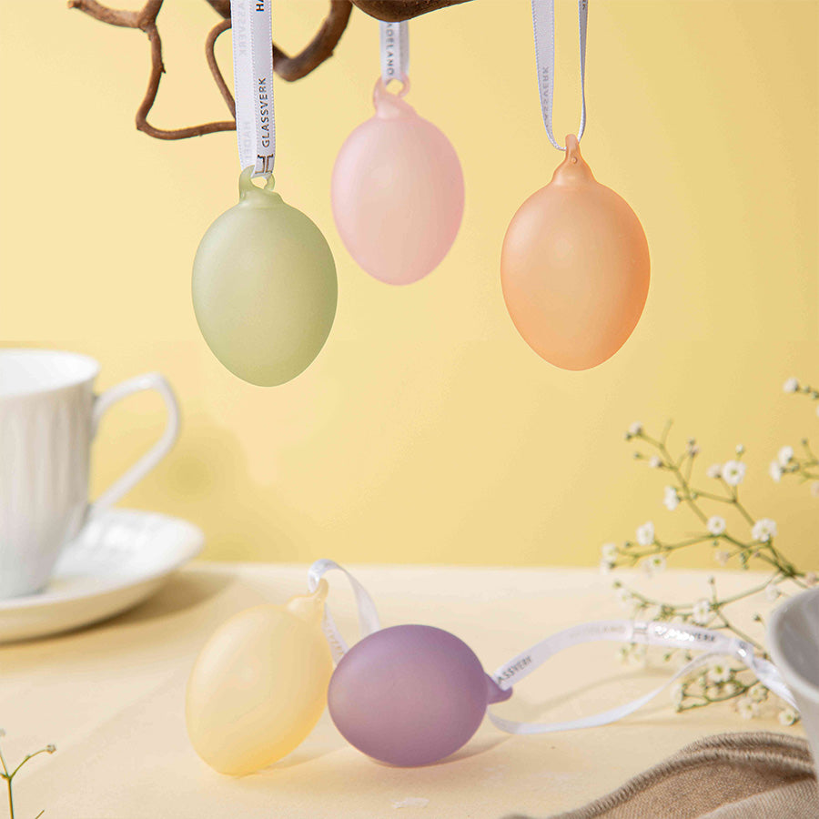 Frostede glassegg i rosa, lilla, lys grønn og gul, dekorativt arrangert på en gren, ideelle for påskepynt.