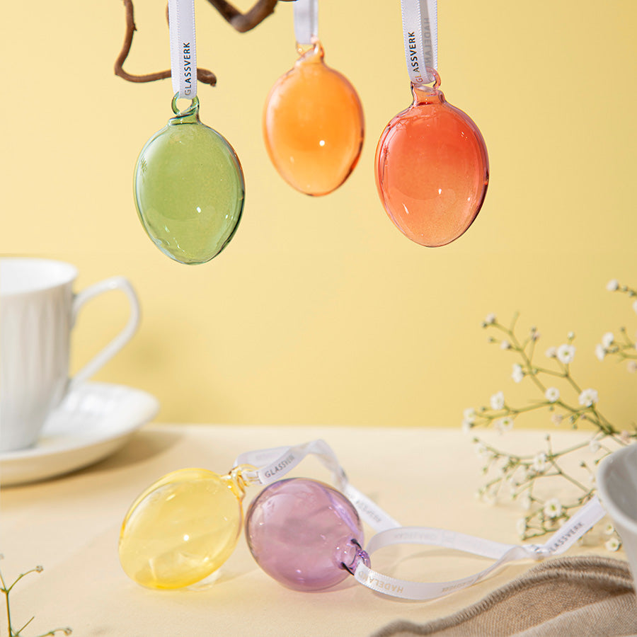 Glassegg i klare, lyse farger henger fra grener i en vase, og illustrerer hvordan Hadeland Glassverk glassegg kan brukes til å pynte i påskedekorasjoner.