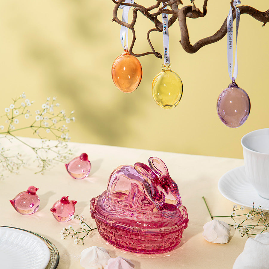 Fargede glassegg kombinert med en rosa glasskanin og blomster, som viser hvordan Hadeland Glassverk glassegg kan tilføre en sofistikert stil til påskeinnredningen.