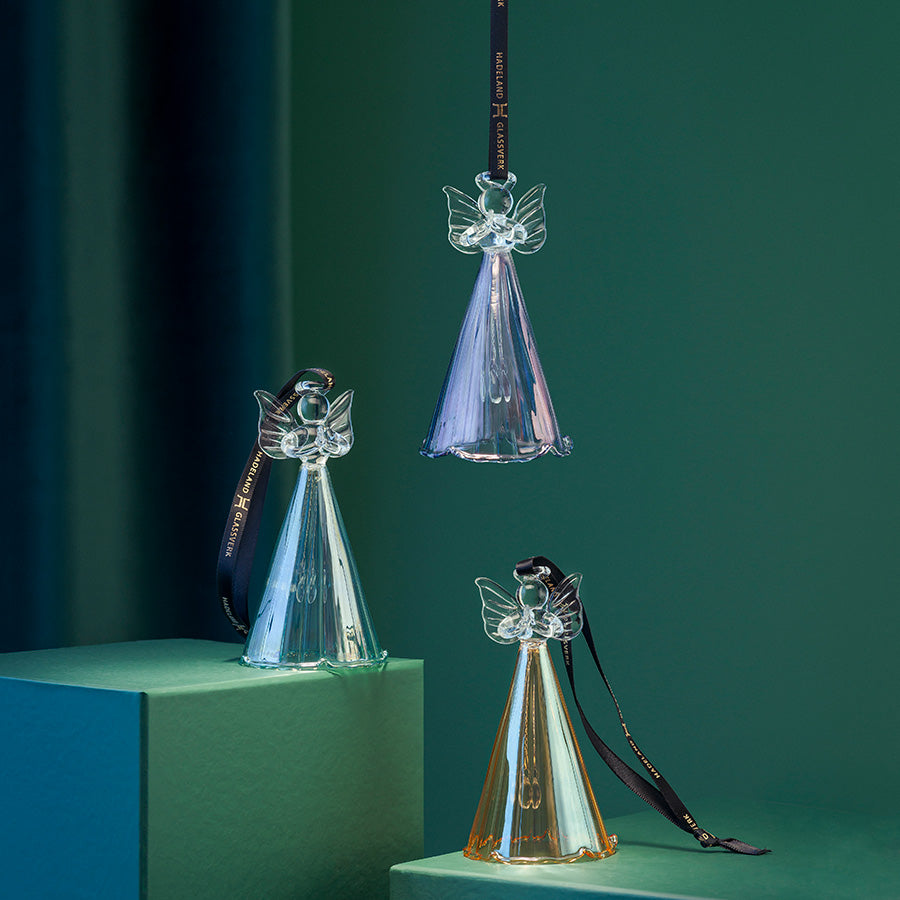 Hadeland Glassverk julepynt bestående av tre glassengler i transparente farger, displayet på grønne overflater. Perfekt for å skape en stemningsfull jul.