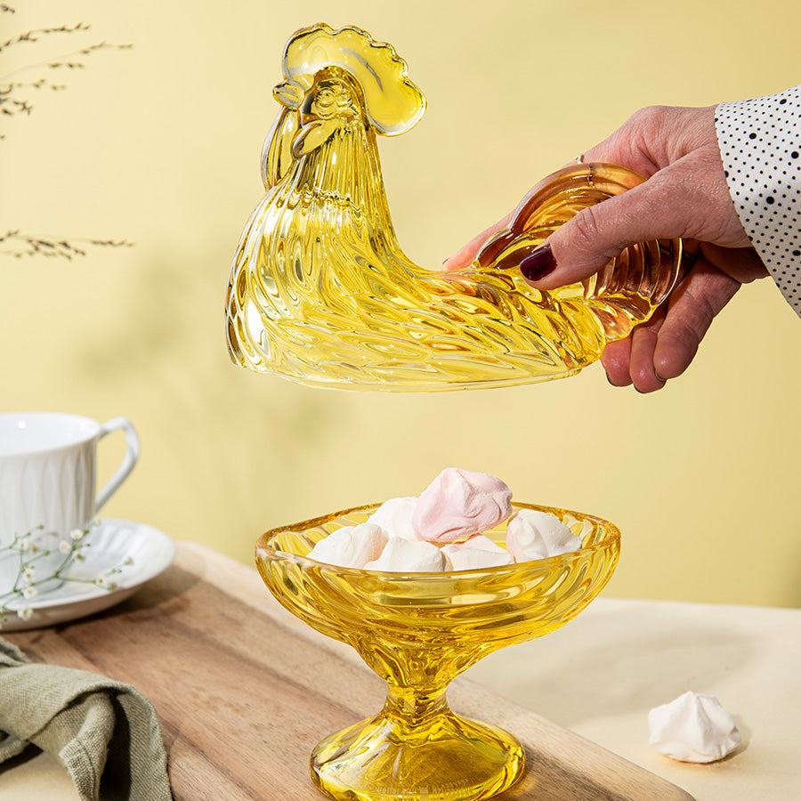 Hendel av glasshane i gullfarget glass, fylt med småkaker, i et stilfullt miljø.
