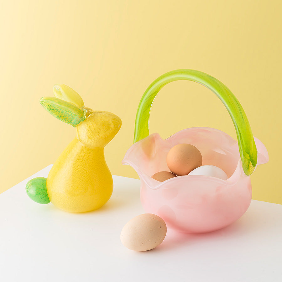 Hadeland Glassverk HG Påske Glasskanin 18cm Gul - glasskanin ved siden av en rosa glasskurv med egg, ideell dekorasjon til påskepynt.