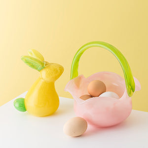 Fargeriktig kombinasjon av en rosa glasskurv med grønt håndtak og en gult påskehare, dekorert med påskeegg.