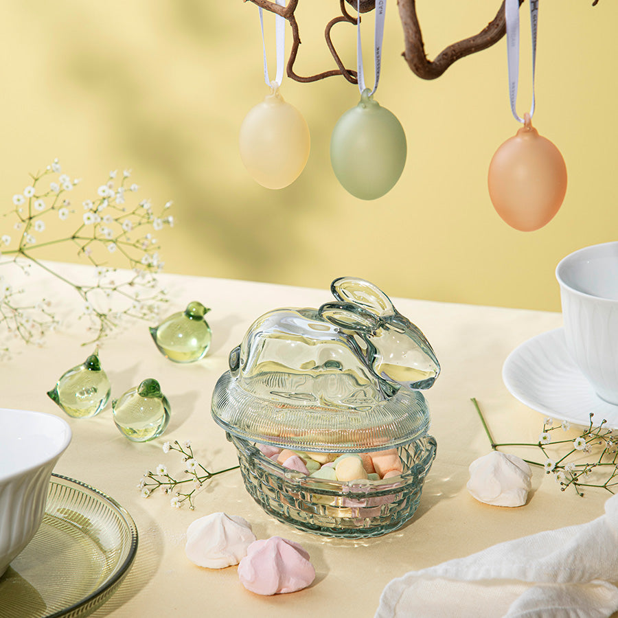 Påskekyllinger i glass plassert på et bord sammen med dekorative påskeelementer.