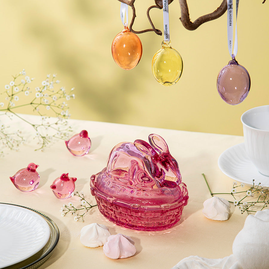 Tre rosa påskekyllinger fra Hadeland Glassverk, sammen med påskeegg, som skaper en festlig påskestemning.