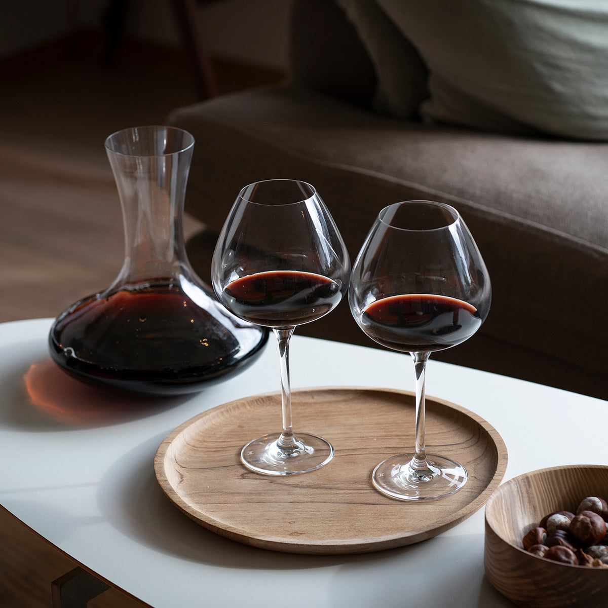 To Hadeland Glassverk Odyssé Rødvinsglass 82cl på et bord med en karaffel og en trefat, perfekt for vinkvelder.