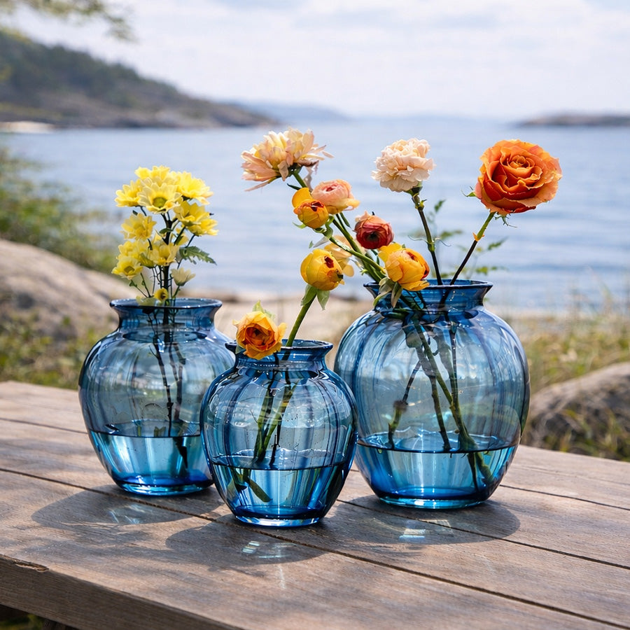 Hadeland Glassverk Emily Vase 17,5cm Blå Optikk presentert i et naturlandskap med blomster, et tidløst tillegg til ethvert hjem.