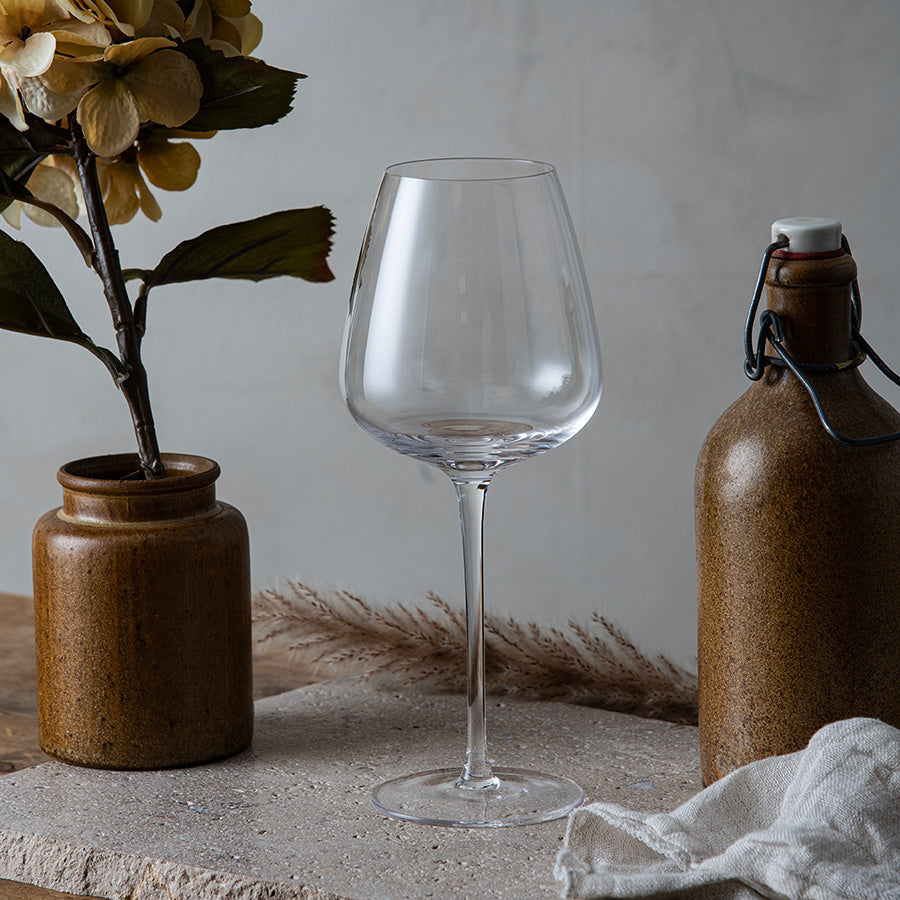 Hadeland Glassverk Odyssé Allroundglass 56cl 6pk plassert på et naturlig bord med brune dekorative elementer, perfekt for å servere både rød- og hvitvin.