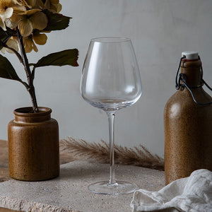 Hadeland Glassverk Odyssé Allroundglass 56cl 6pk plassert på et naturlig bord med brune dekorative elementer, perfekt for å servere både rød- og hvitvin.