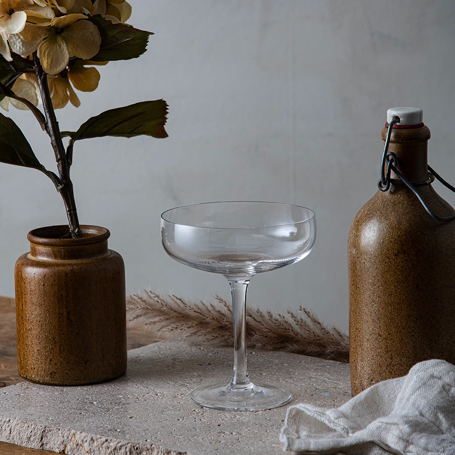 Hadeland Glassverk Odyssé Cavaskål 25cl 6pk plassert dekorativt ved siden av en blomstervase og keramikkpotte. En stilfull glasskål ideell for servering av cava og musserende vin.