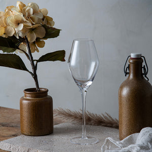 Elegant Hadeland Glassverk Odyssé champagneglass 32 cl i en dekorativ setting med blomster og keramiske beholdere, perfekt for å fremheve aroma og bobler av champagne.