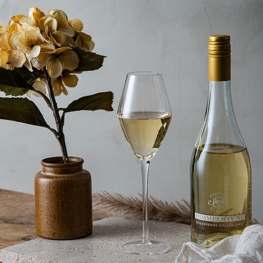 Hadeland Glassverk Odyssé champagneglass 32 cl fylt med musserende vin, plassert ved siden av en vinflaske, perfekt for festlige anledninger og tidløs eleganse.