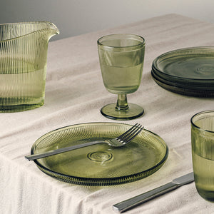 Hadeland Glassverk Siri glass med stett i grønn farge sammen med tallerkener, illustrerer tidløs design og elegant bordoppsett.