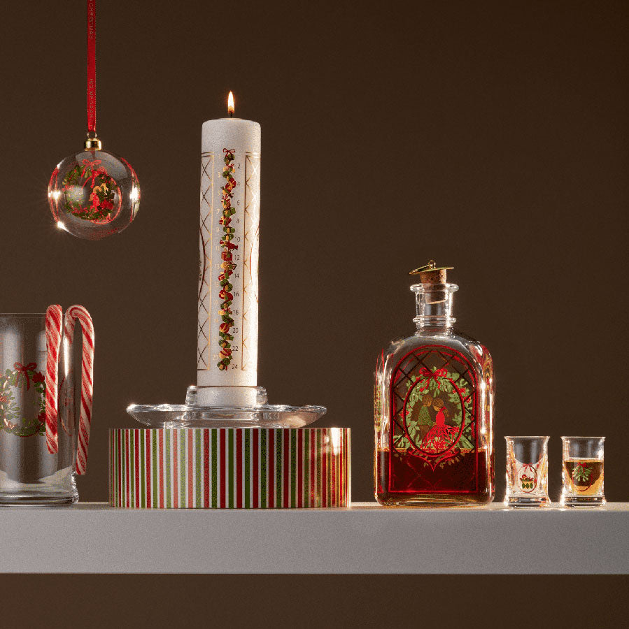 Holmegaard Christmas Juledrammeglass 2025 i en dekorativ setting med julepynt, lys og drikkeflaske, som skaper en koselig julestemning.