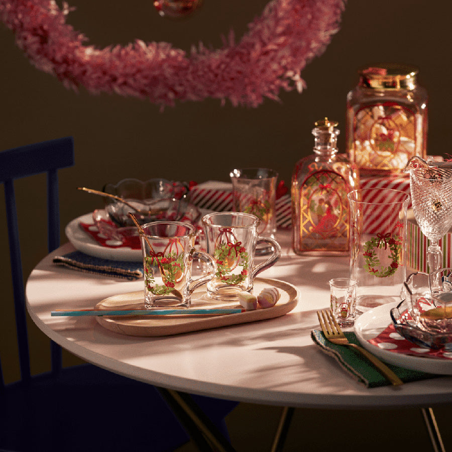 Holmegaard Christmas Hotdrink Juleglass 2025, 23 cl, satt på et festlig dekket bord med julekledde glass, småkaker, og julestemning i luften, fremhever dansk håndverk og nostalgisk julefeiring.