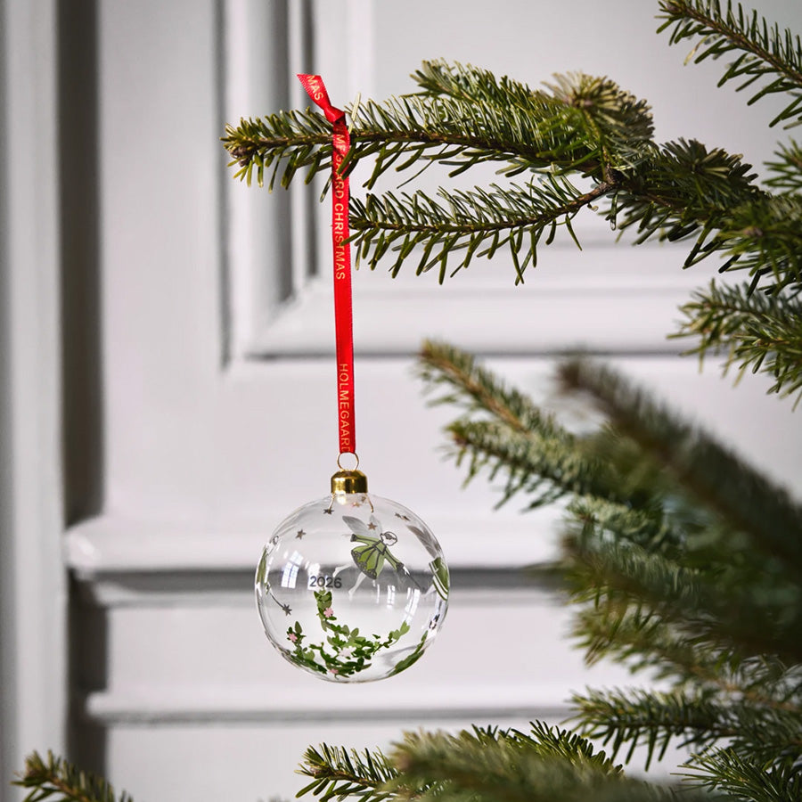 Holmegaard Christmas 2026 julekule i glass henger dekorativt på et juletre med rødt silkebånd