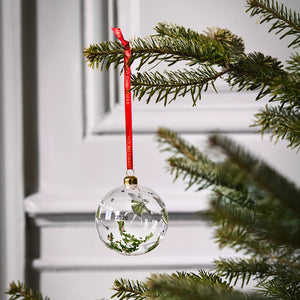 Holmegaard Christmas 2026 julekule i glass henger dekorativt på et juletre med rødt silkebånd