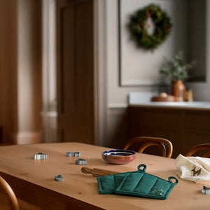 Julegrønn JUNA Christmas Fable gryteklut med brodert juletre på kjøkkenbordet, sammen med annet juleinspirert kjøkkentilbehør.